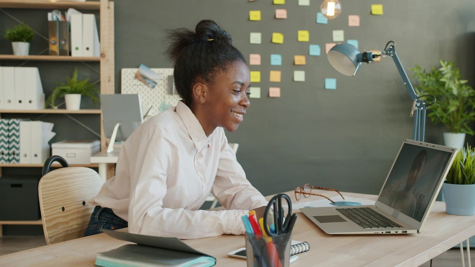 A woman at a desk smiles at her laptop during a video call.